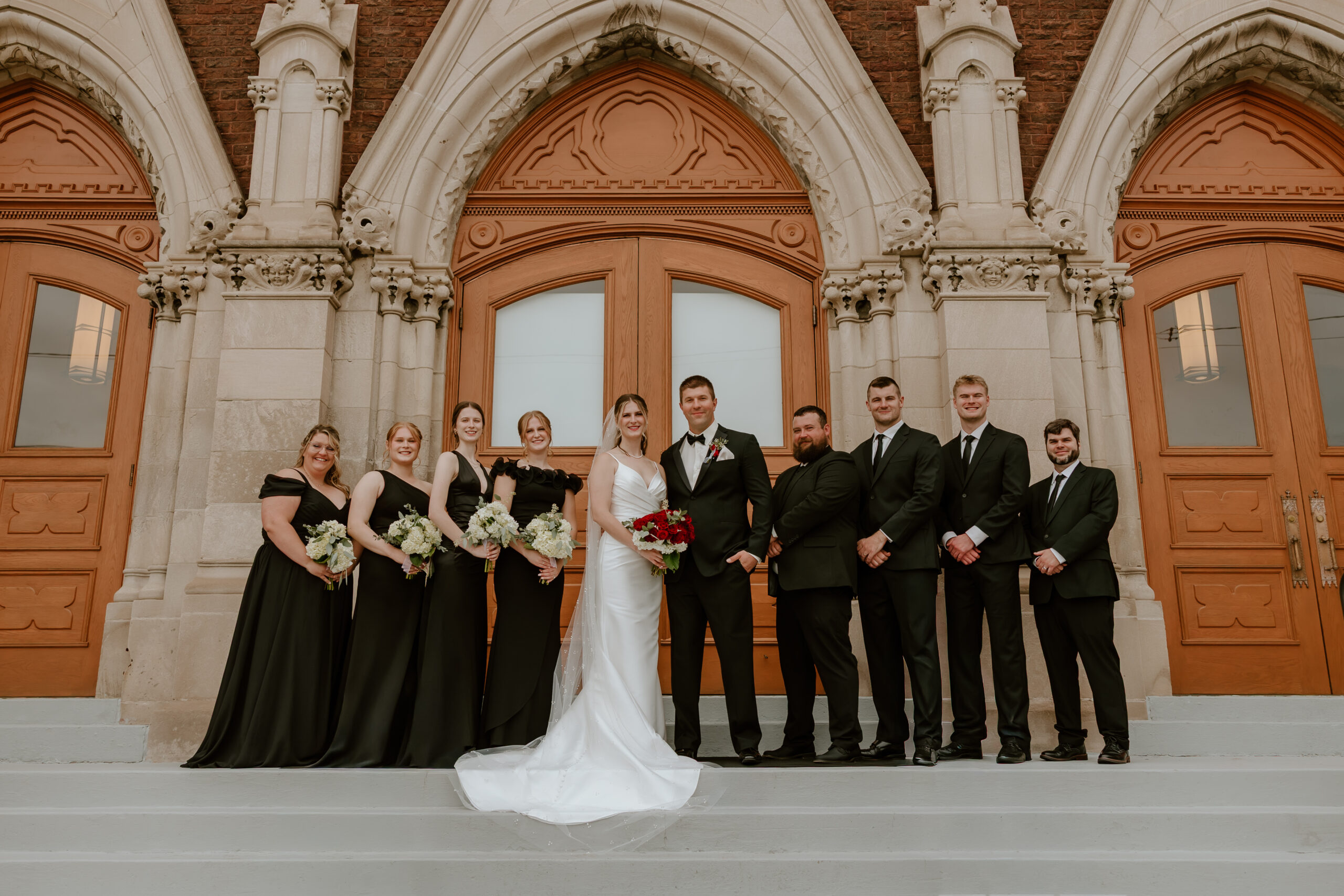 A bridal party stands in a line in front of a church.